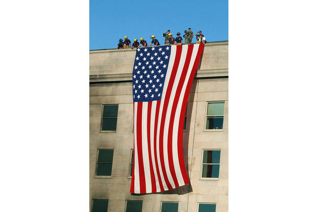 Soldiers from the 3rd Infantry Regiment (The Old Guard) render honors as firefighters and rescue workers unfurl a huge American flag over the side of the Pentagon while rescue and recovery efforts continued following the Sept. 11, 2001, terrorist attack. The garrison flag, sent from the U.S. Army Band at nearby Fort Myer, Virginia, is the largest authorized flag for the military. (Navy photo by Petty Officer 1st Class Michael Pendergrass)