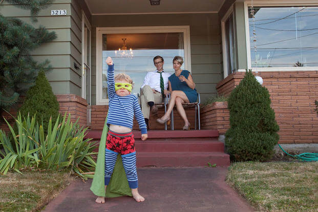 Young parents at home with son dressed as superhero