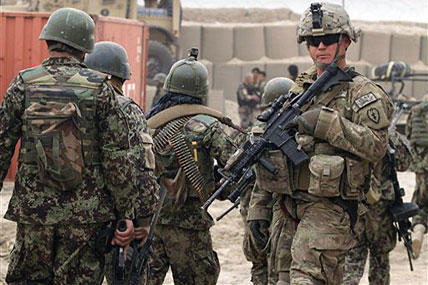 Afghan soldiers, left, walk past a U.S. Army soldier outside of a military base in Panjwai, Kandahar province south of Kabul, Afghanistan.