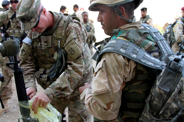 Col. Michael Midkiff helps an Iraqi soldier unwrap an M16A2 rifle he received at Camp Taji, Iraq. (Photo by Capt. A. Sean Taylor, 310th A&A, CJTF-OIR Public Affairs)