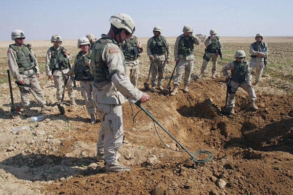 U.S. soldiers watch as a mine sweeper looks for weapons in a hole they dug during a raid on a farm just outside Tikrit, Iraq, on Oct. 9, 2003. (AP)