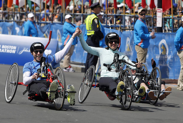 Boston Marathon husband and wife bombing survivors Patrick Downes and Jessica Kensky, who each lost a leg in last year's bombings, roll across the finish line in the 118th Boston Marathon Monday, April 21, 2014 in Boston. (AP Photo/Elise Amendola)