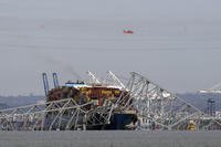 A helicopter flies over a container ship as it rests against wreckage of the Francis Scott Key Bridge