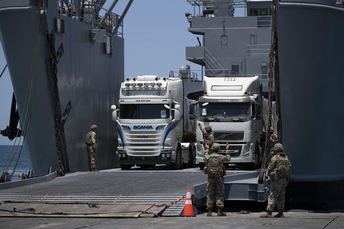 U.S. Army soldiers gesture as trucks loaded with humanitarian aid arrive at the U.S.-built floating pier Trident