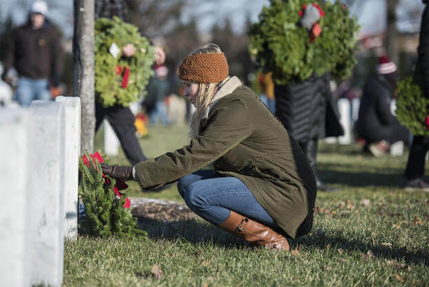 A volunteer place wreaths at a headstone in Section 60 during the Wreaths Across America event at Arlington National Cemetery, Arlington, Virginia, Dec. 16, 2017. (U.S. Army/Elizabeth Faser).