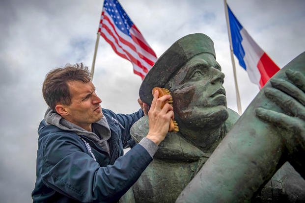 Navy Petty Officer 1st Class Jacob Smelser cleans a monument at the Utah Beach D-Day Museum in Sainte-Marie-du-Mont, France, April 10, 2018, during a port visit by the USS Porter. (Navy photo by Petty Officer 3rd Class Ford Williams)