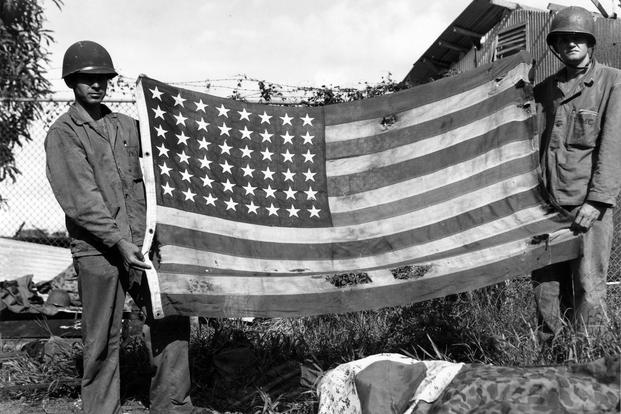Marines display the American flag for a photograph shortly after securing a beachhead during the liberation of Guam, July 21, 1944. (John Raufmann/U.S. Marine Corps photo)