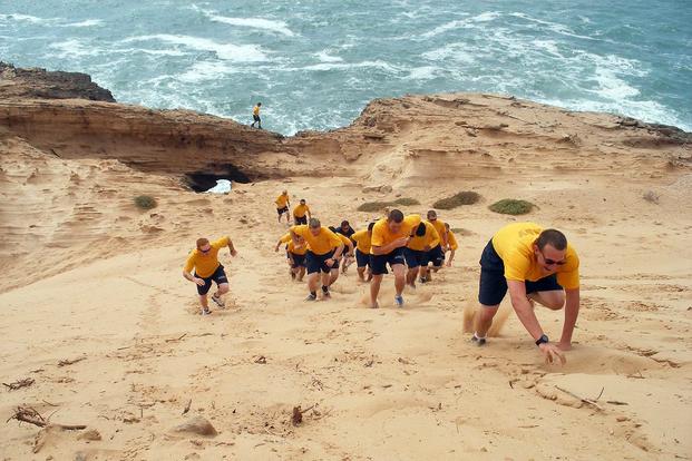 Seabees run up a sand dune.