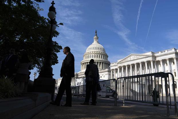 The U.S. Capitol is seen as people walking on the sidewalk with a fence