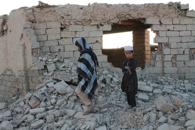 Afghan boys walk near a damaged house.
