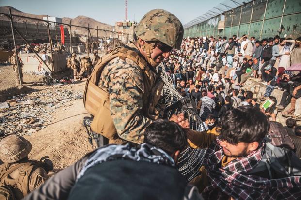 A Marine assists evacuees at an Evacuation Control Check Point at Hamid Karzai International Airport.