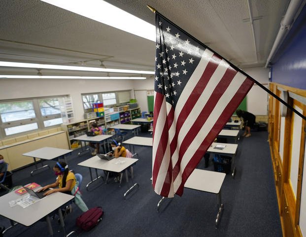 An American flag is in a classroom as students work on laptops