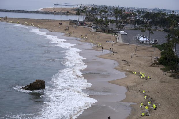 Workers in protective suits clean the contaminated beach in California