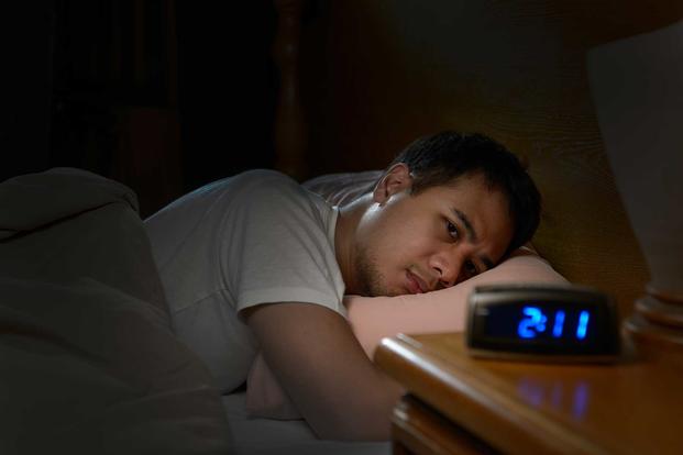 Man laying in bed staring at clock which reads 230 AM