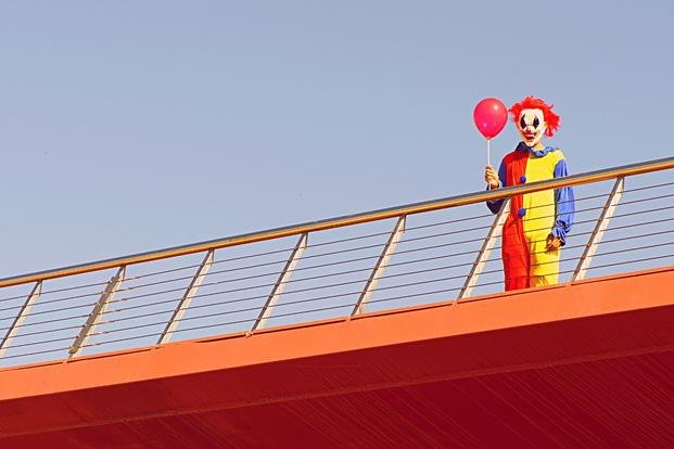 creepy clown with red balloon looms on bridge