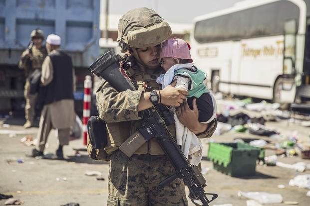 A Marine holds a baby while a family in-processes at Hamid Karzai International Airport, Kabul, Afghanistan.