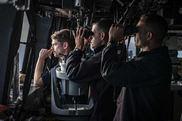 U.S. Navy officers scan the horizon from the bridge of the USS Green Bay