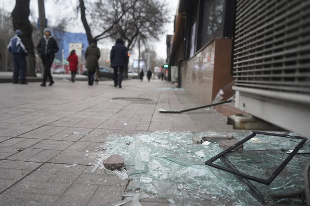 People walk past a shop with broken  windows in Almaty, Kazakhstan