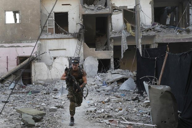 A U.S.-backed Syrian Democratic Forces fighter runs in front of a damaged building in Raqqa, Syria.