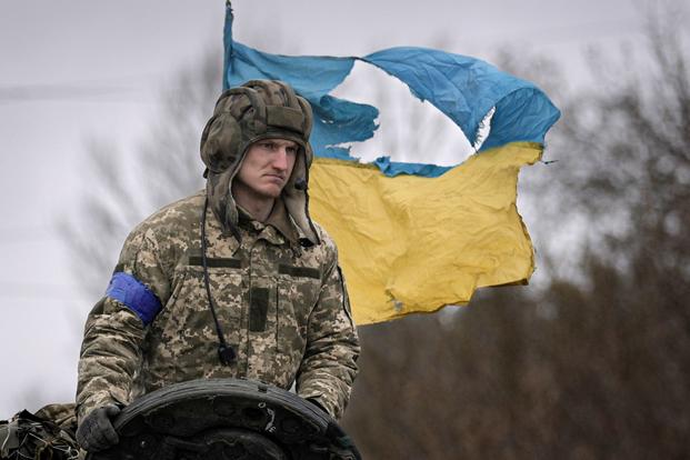 A Ukrainian serviceman is backdropped by his country's flag outside Kyiv, Ukraine.