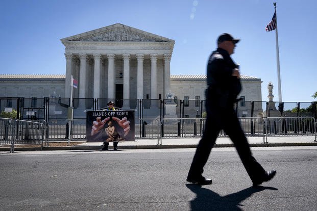 A Colorado man holds a sign saying "hands off Roe" as a Capitol police officer walks past barricades outside of the Supreme Court.