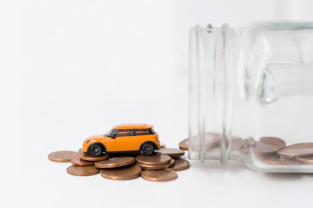 Photo of a toy car on top of a pile of pennies outside a jar