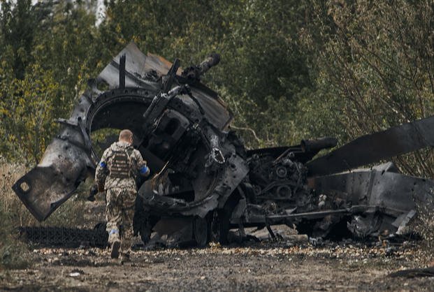 A Ukrainian soldier passes by a Russian tank damaged in a battle.