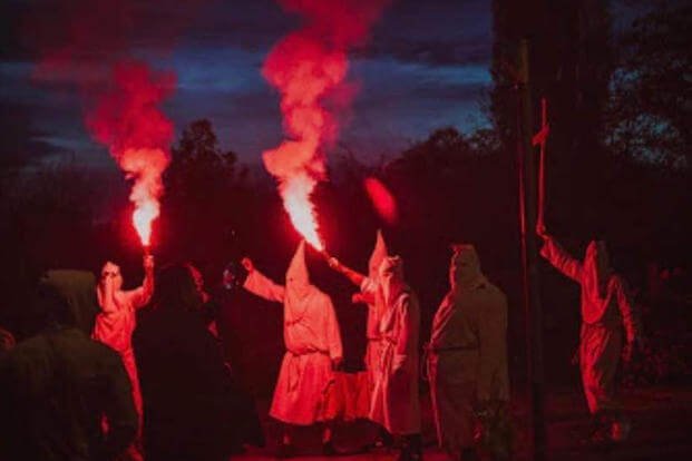 Several men dressed as klansmen lighting red flares, a staple of far-right protests in Europe. 