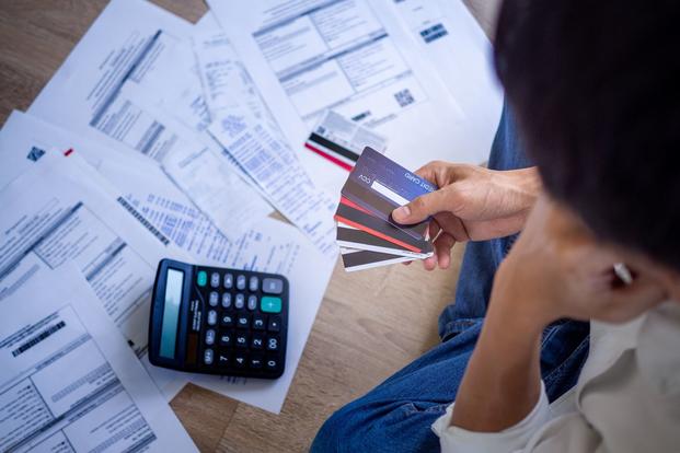 A person holding a stack of credit cards looks at stacks of papers.