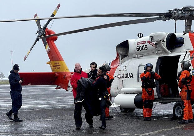 Coast Guard personnel help carry a swimmer from a rescue helicopter after he was rescued