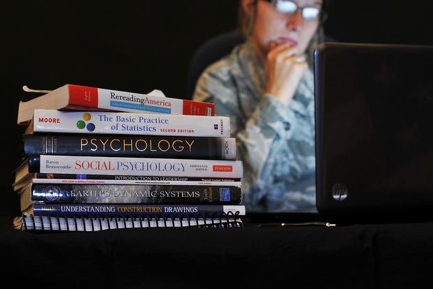 A service member sits near a stack of textbooks.
