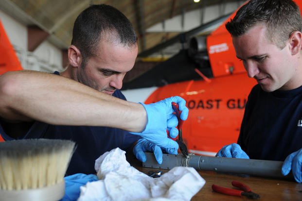 U.S. Coast Guard Petty Officer 2nd Class Yusef Vera (left) performs routine repairs on flight controls for the MH-65A HITRON Helicopter at the Naval Station Guantanamo Air Terminal, Cuba.