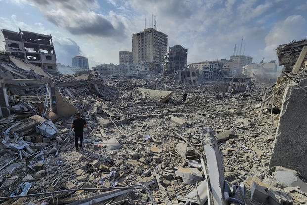 Palestinians walk through buildings destroyed by Israeli airstrikes
