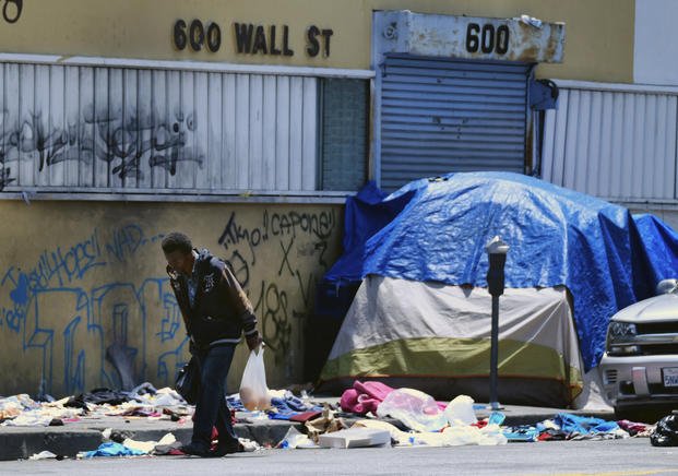 Homeless man walks along a street lined with trash in downtown Los Angeles