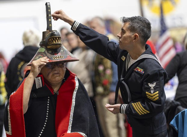 A member of the U.S. Navy sprinkles tobacco on top of a killer whale clan hat