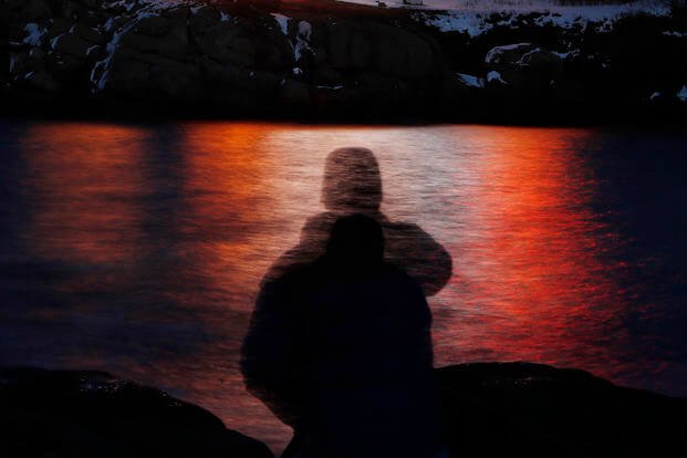 A man is silhouetted against lights reflected in the waters off Cape Neddick in Maine.