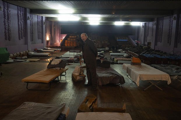 A man waits for evacuation to western Ukraine as he stands by a bed in a city theatre