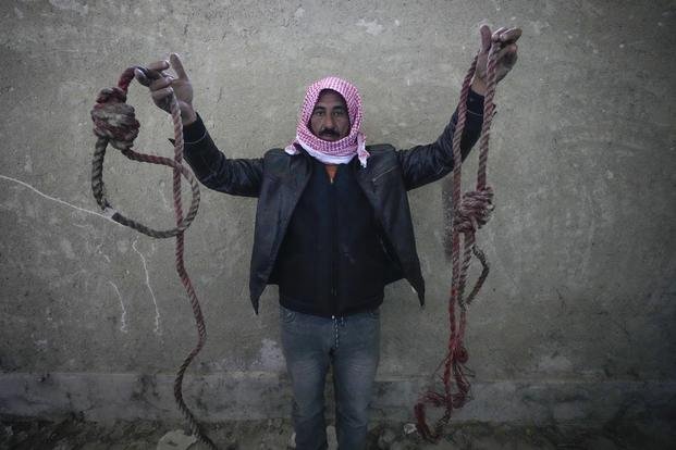 A man holds up two ropes tied in the shape of nooses, found in the infamous Saydnaya military prison