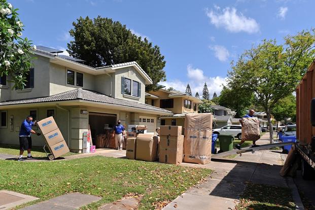 Packed boxes are stacked outside military family housing while movers move things around.