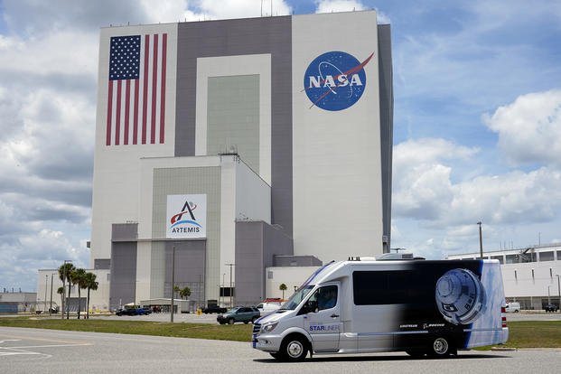 NASA astronauts Butch Wilmore and Suni Williams, riding in the astro van, drive by the Vehicle Assembly Building on the way back to the operations and checkout building after a launch was scrubbed in Cape Canaveral, Fla.