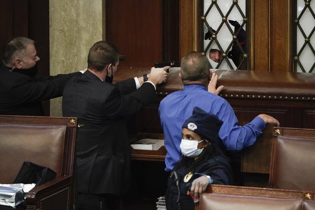 Police with guns drawn watch as rioters try to break into the House Chamber