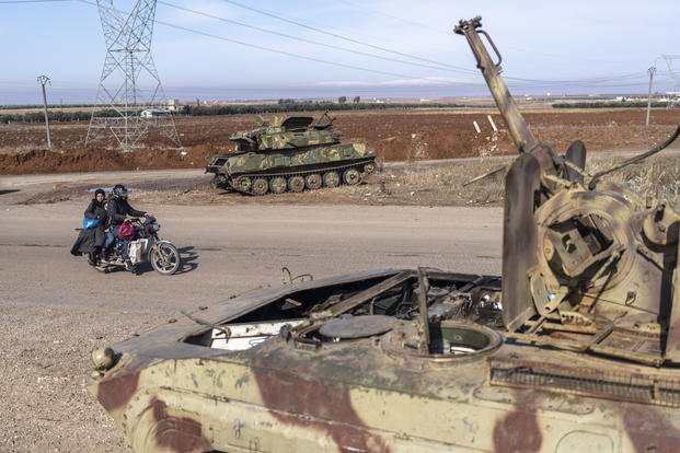 A family drives past tanks that belonged to the Assad regime, in Nawa, near Daraa, Syria