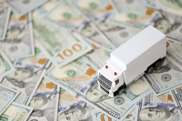 A toy moving truck is on top of scattered U.S. $100 bills.