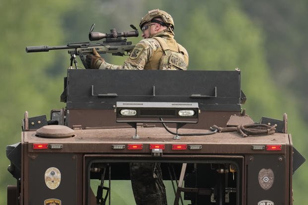 A law enforcement officer trains his rifle towards a house as the officers search for shooting suspect Vance Boelter