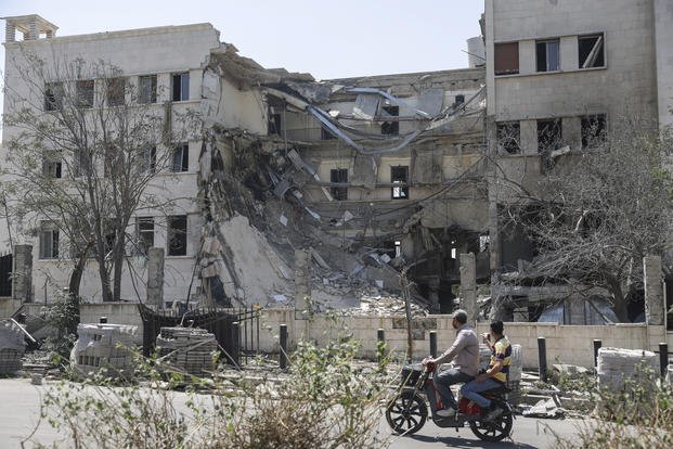 People pass in front of the Syrian Defense Ministry building which on Wednesday was heavily damaged by Israeli airstrikes in Damascus, Syria