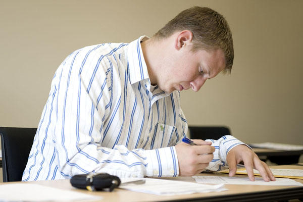 Man writing at a desk wearing a collared shirt.