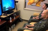 U.S. Air Force Gen. Mike Holmes, the commander of Air Combat Command, and 1st Lt. Wade Holmes, his son, battle each other in a combat flight action video game June 29, 2019, at Joint Base Langley-Eustis, Virginia. (U.S. Air Force/Emerald Ralston)