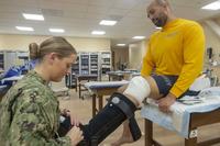 A Navy orthopedic technician applies a controlled ankle motion booth to a sailor