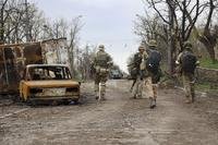 Servicemen of Donetsk People's Republic militia walk past damaged vehicles.