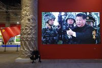 A man rests next a video screen showing Chinese President Xi Jinping.